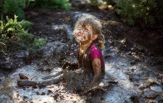 A little girl smiling up at the sun, covered in her favorite mud puddle.