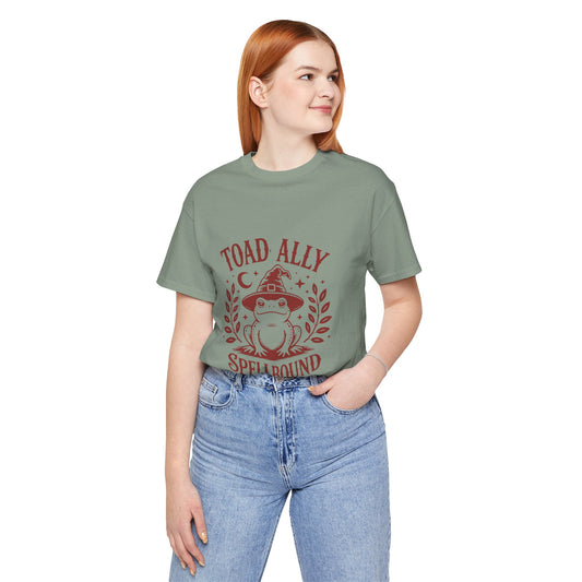 Sage tee printed with a toad in a witch hat inside a leaf wreath, surrounded by a moon and stars, reading "TOAD ALLY SPELLBOUND".