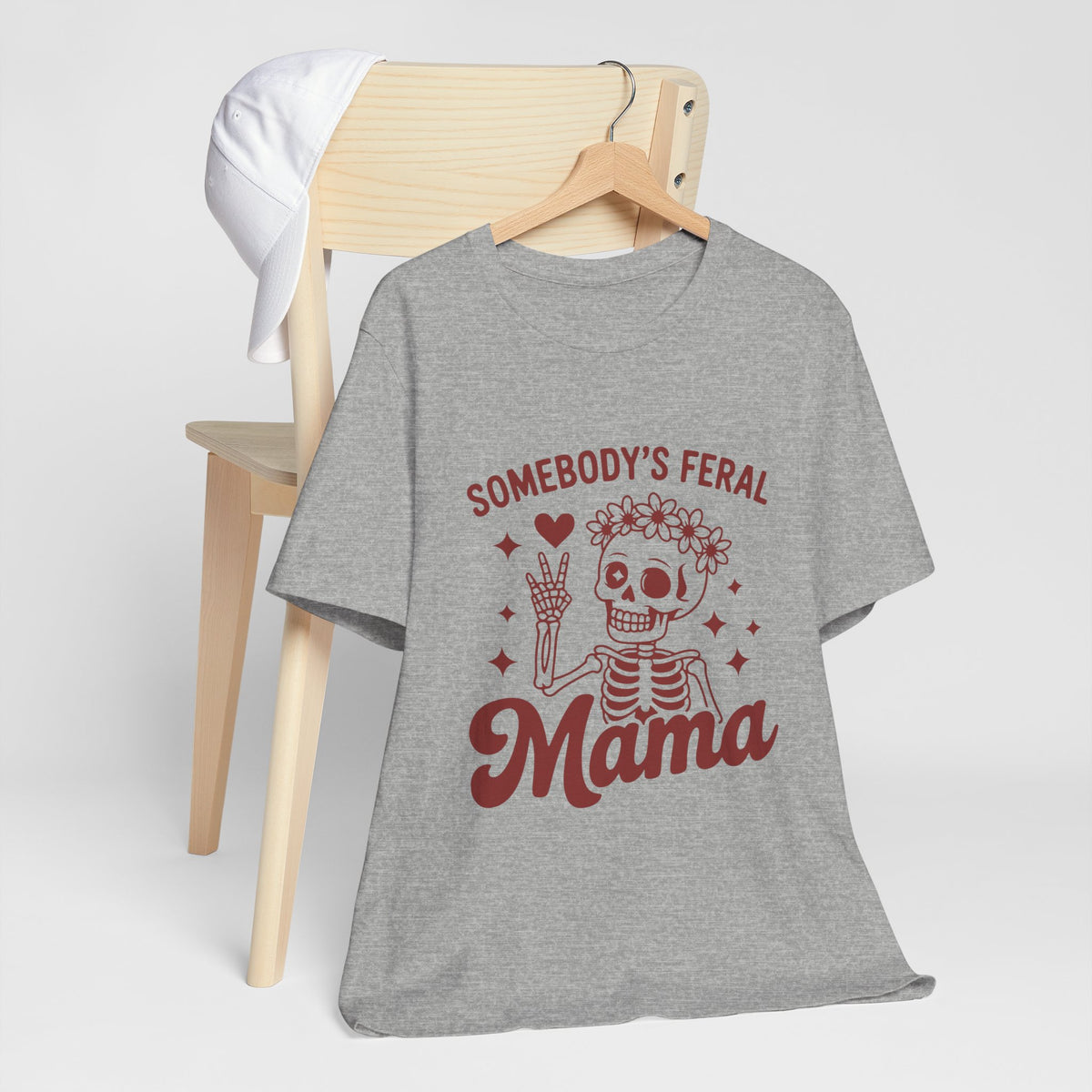 Athletic Heather tee printed with a flower-crowned skeleton giving a peace sign, reading "SOMEBODY'S FERAL MAMA".