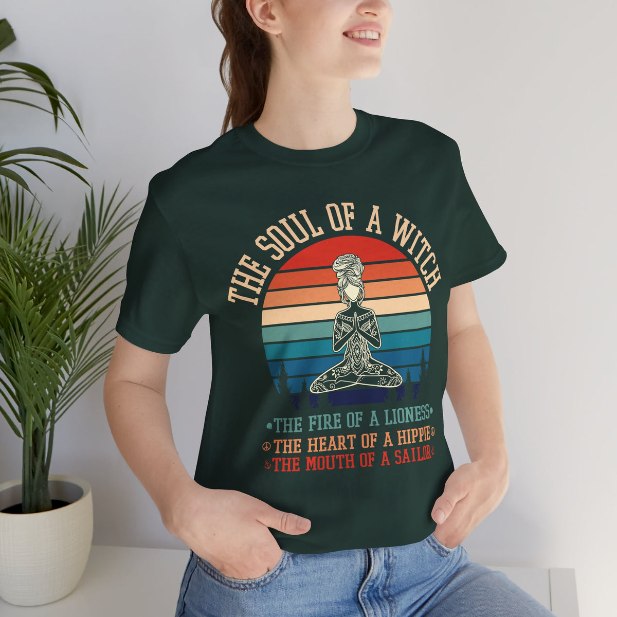 A woman modeling a forest short-sleeve t-shirt with a retro sunset graphic of a woman in lotus pose drawn in mandala linework, reading ‘THE SOUL OF A WITCH, THE FIRE OF A LIONESS, THE HEART OF A HIPPIE, THE MOUTH OF A SAILOR’.