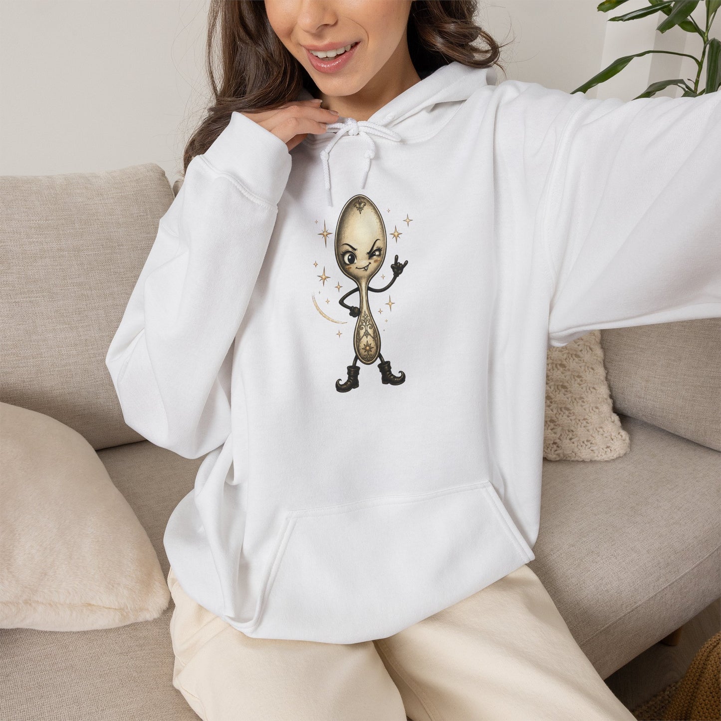 A woman wearing a white hoodie with a cartoon spoon graphic on the chest, sitting on a beige couch.
