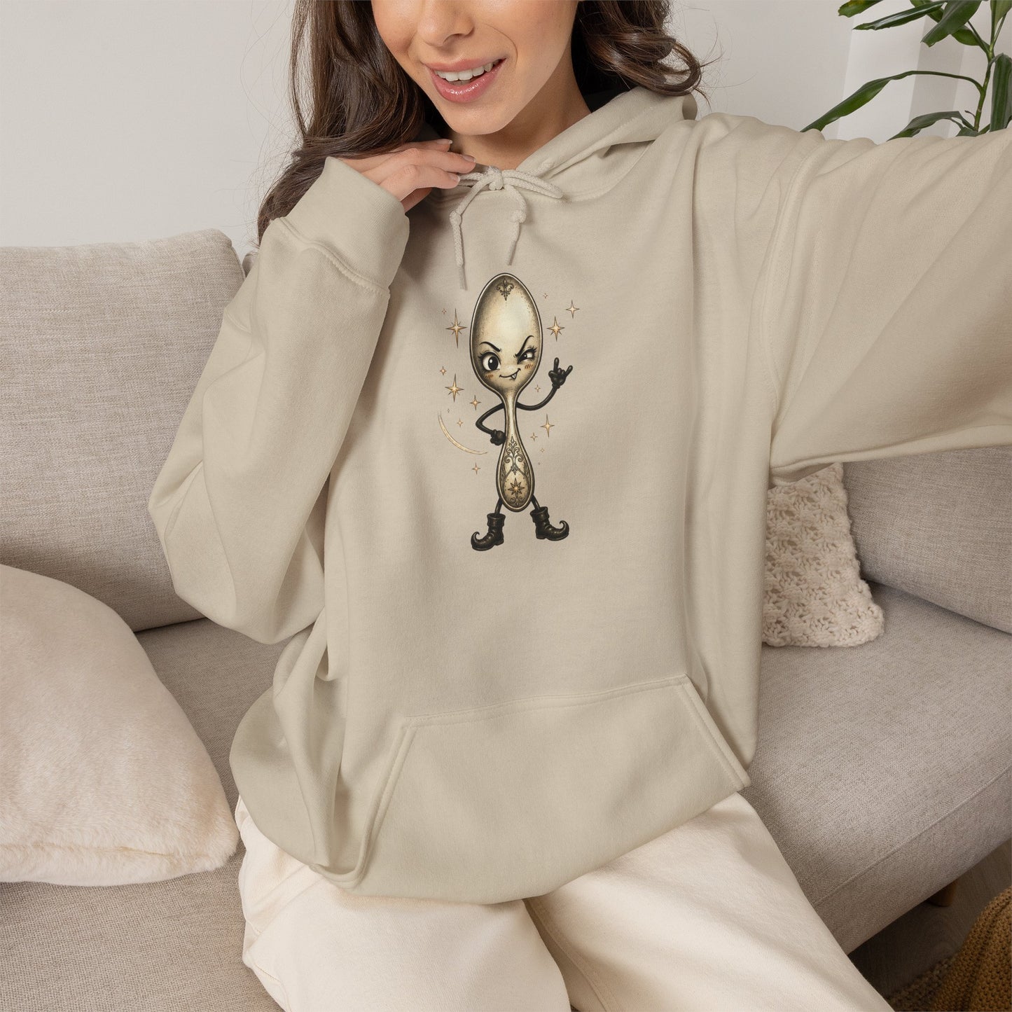 A woman wearing a beige hoodie with a cartoon spoon graphic on the chest, sitting on a beige couch.
