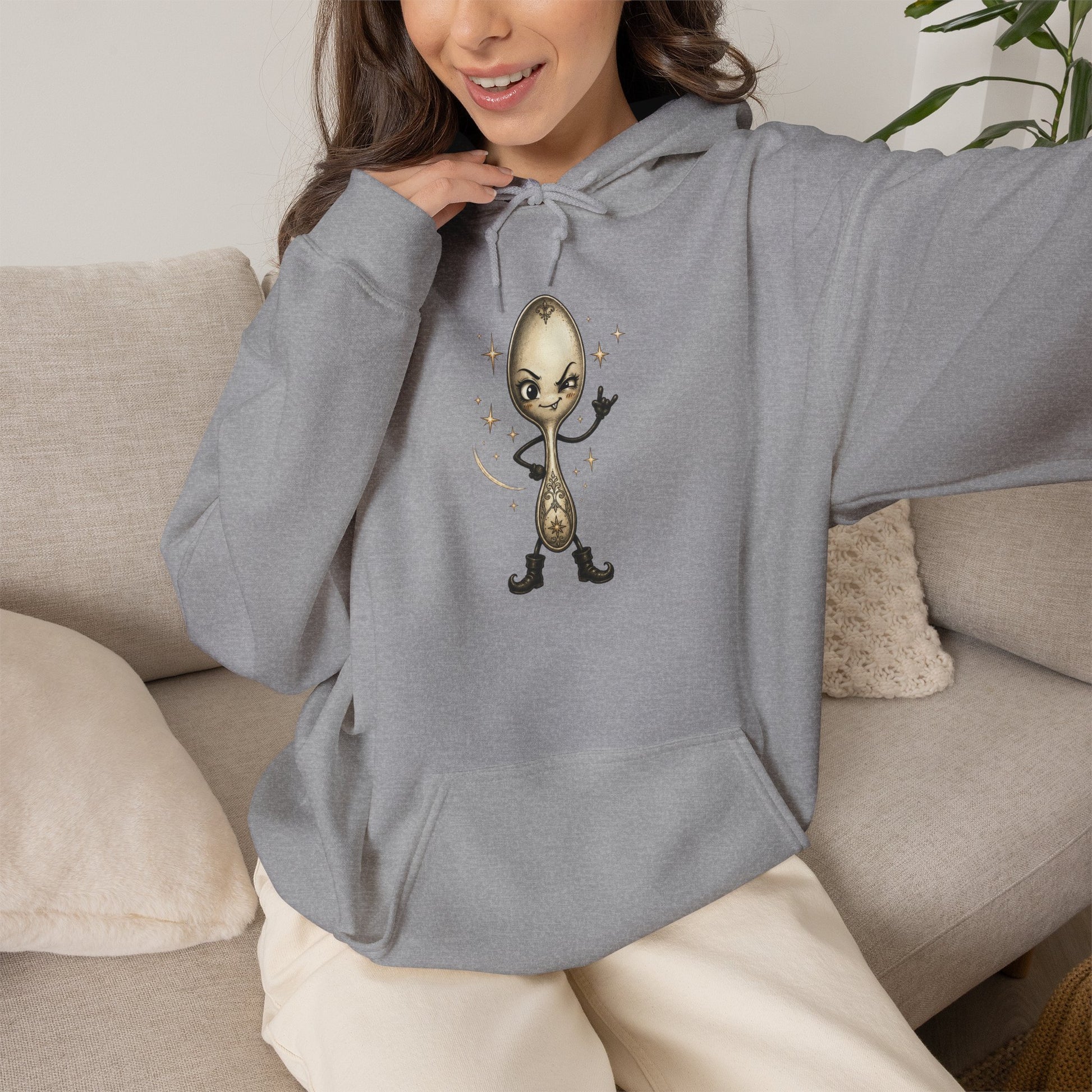 A woman wearing a light grey hoodie with a cartoon spoon graphic on the chest, sitting on a beige couch.