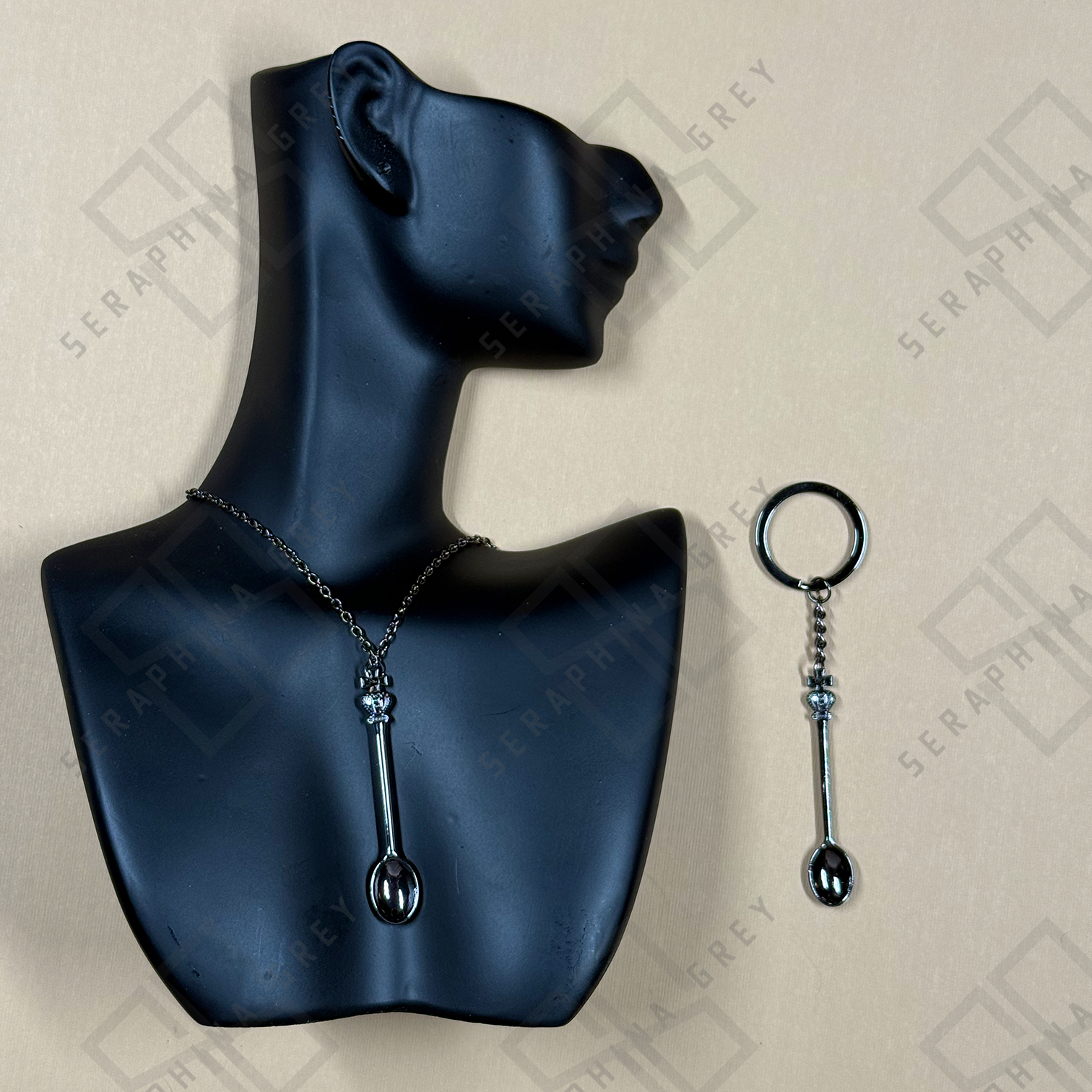 Black necklace and keychain with spoon design on a blue mannequin bust and light gray background.
