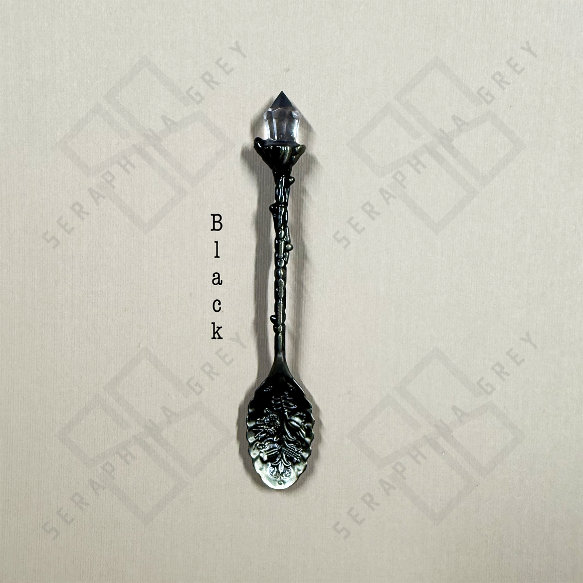 Black colored crystal tipped spoon on cream background