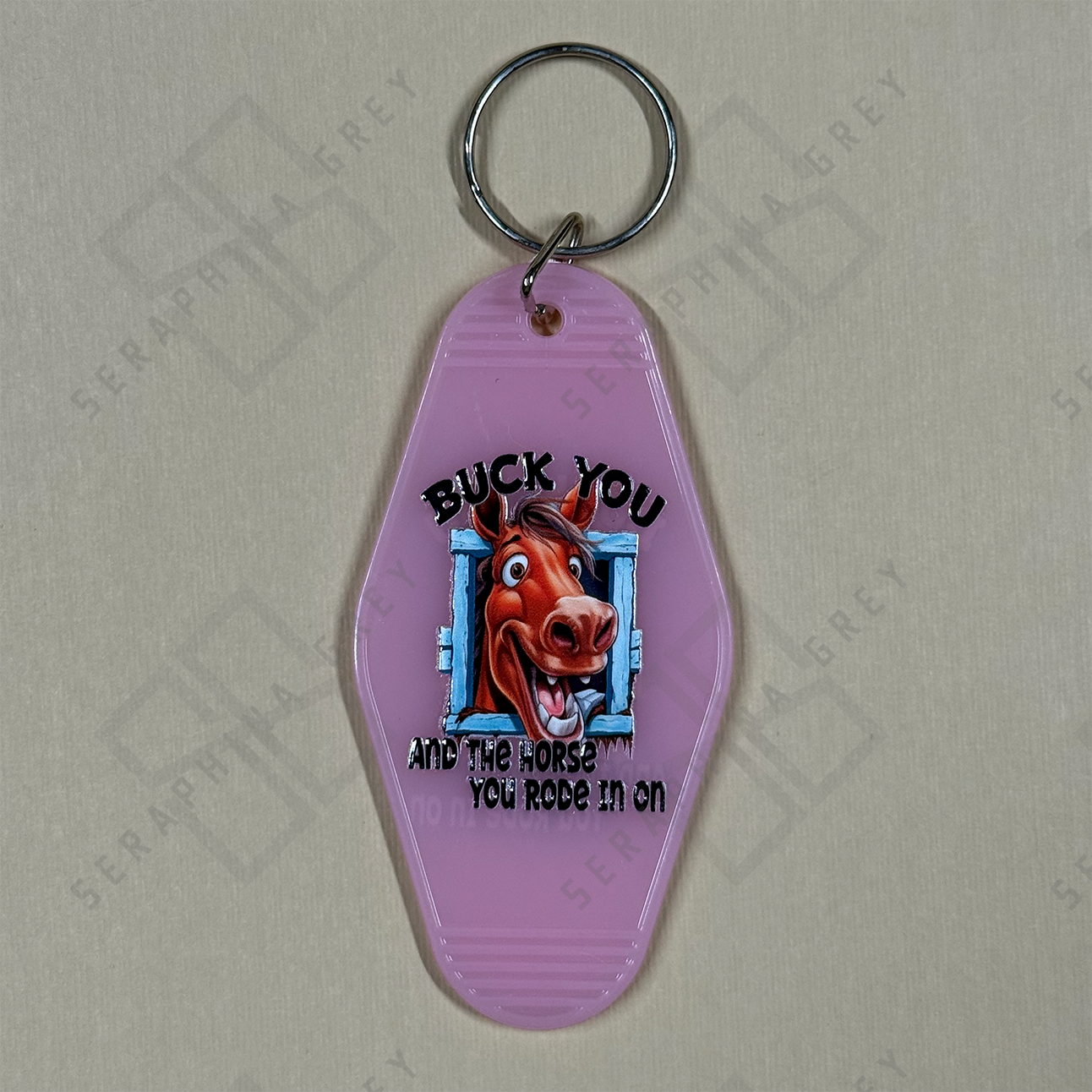 Pink keychain with a horse graphic and text Buck you and the horse you rode in on.