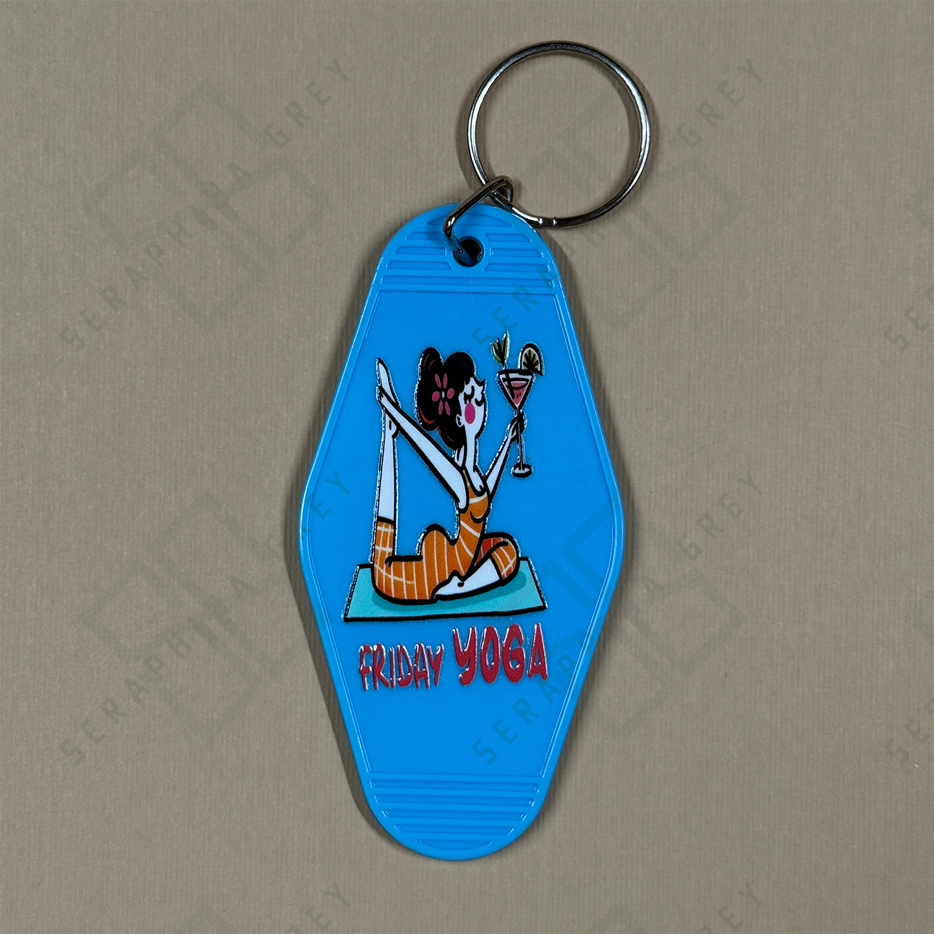 Blue keychain with a cartoon character doing yoga and holding a martini, labeled 'Friday Yoga', on a beige background.
