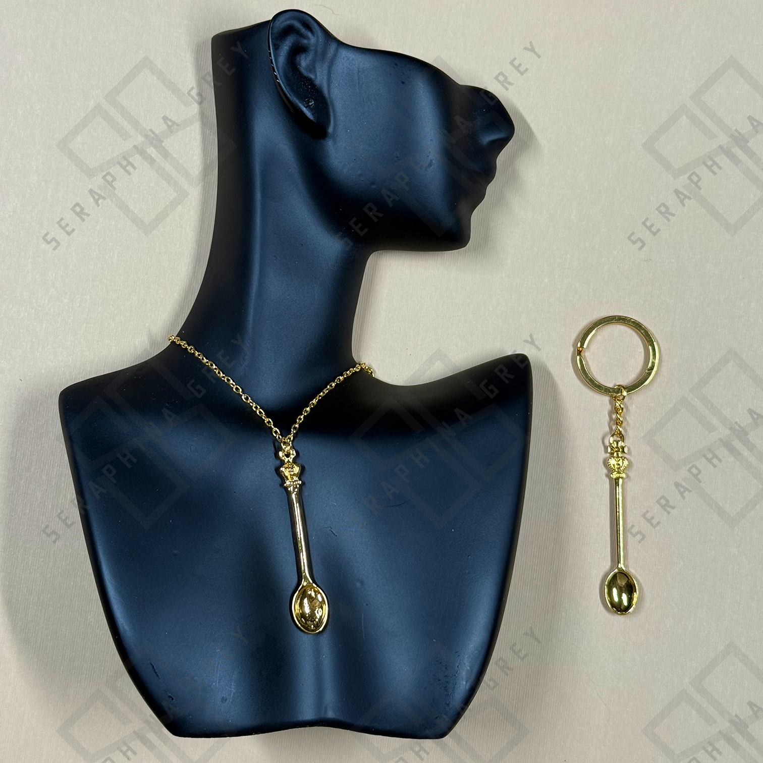 Gold necklace and keychain with spoon design on a blue mannequin bust and light gray background.