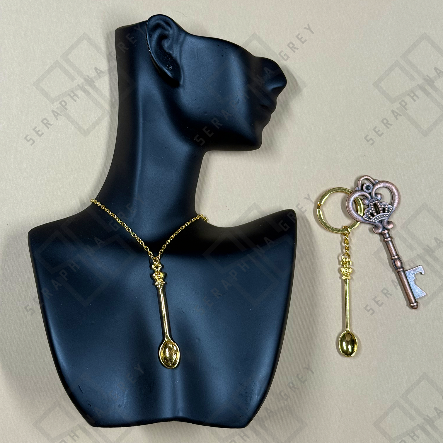 Gold spoon-shaped necklace on a black mannequin bust with matching keychain on a light gray background.