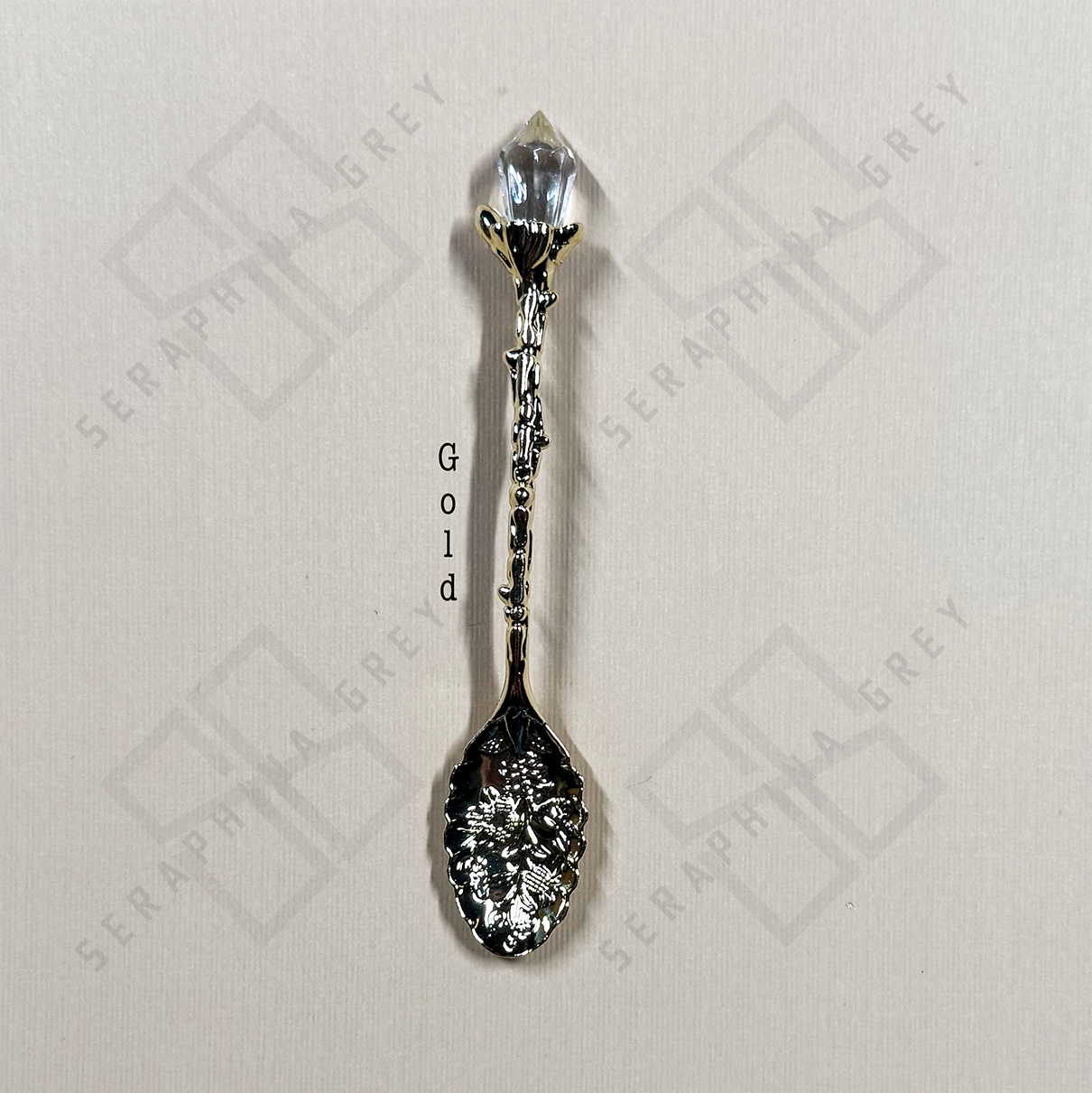 Gold colored crystal tipped spoon on cream background