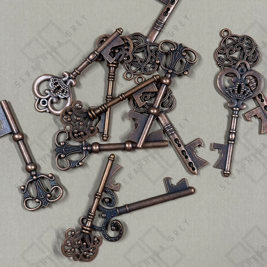 Assorted antique-style bronze skeleton key bottle openers in multiple ornate designs, arranged on a neutral background to show the variety of Grey Street keys available.