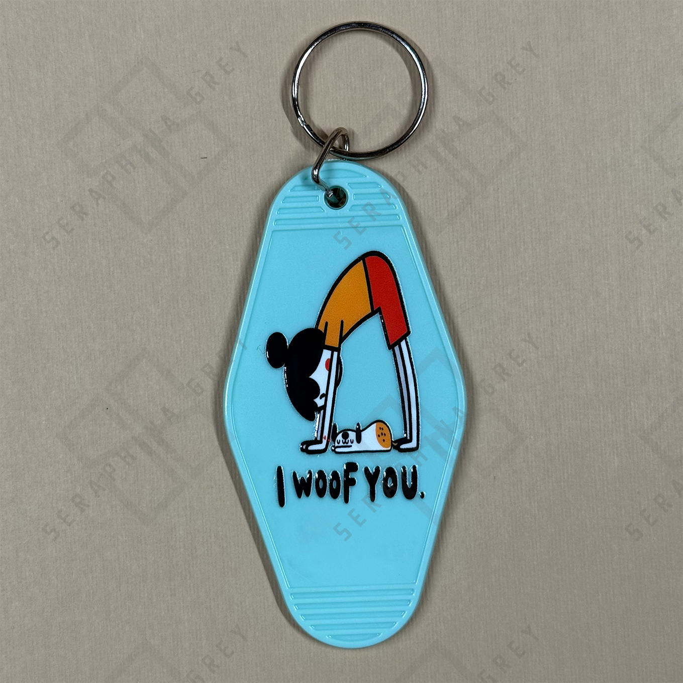 Keychain with a cartoon dog doing yoga pose and 'I woof you' text on a light blue background