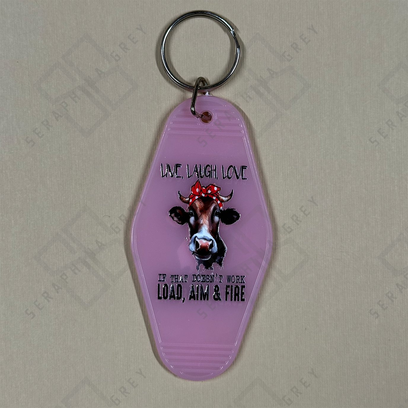 Pink keychain with cow design and text Live Love Laugh if that doesnt work Load Aim Fire.