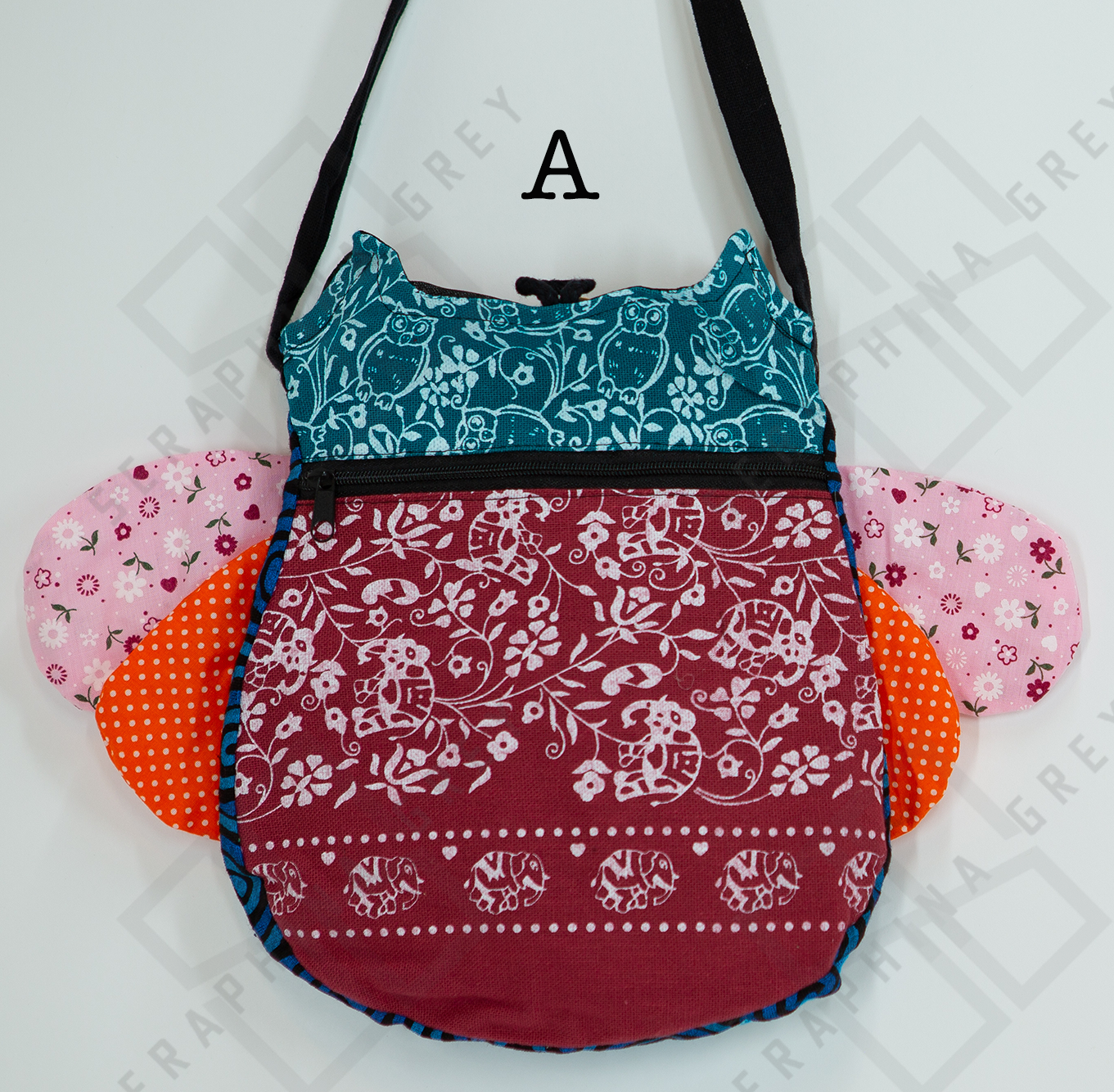 The image shows the back of a colorful handmade round owl handbag labeled “A.” The top half of the bag is green with a white floral and owl pattern, while the bottom half is maroon with a white floral elephant design. The bag has a black zipper running horizontally across the middle. The owl’s pink floral and orange polka-dotted wings are visible on the sides. The bag is hung by a black strap against a white background, showcasing its playful and intricate design.