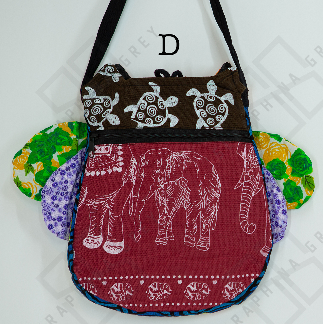 The image shows the back of a colorful handmade round owl handbag labeled “D.” The top half of the bag is brown with a white turtle pattern, while the bottom half is maroon with a white elephant design. The bag has a black zipper running horizontally across the middle. The owl’s green floral and purple polka-dotted wings are visible on the sides. The bag is hung by a black strap against a white background, highlighting its unique and playful design.