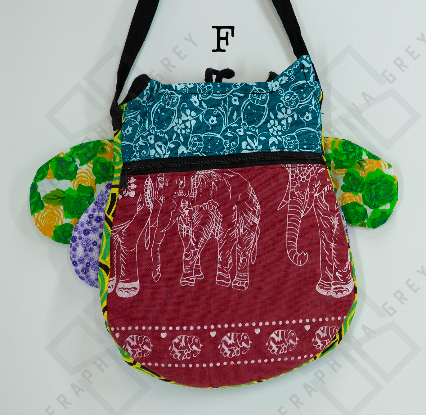 The image shows the back of a colorful handmade round owl handbag labeled “F.” The top half of the bag is blue-green with a white floral and owl pattern, while the bottom half is maroon with a white elephant design. The bag has a black zipper running horizontally across the middle. The owl’s green floral and purple polka-dotted wings are visible on the sides. The bag is hung by a black strap against a white background, highlighting its unique and playful design.