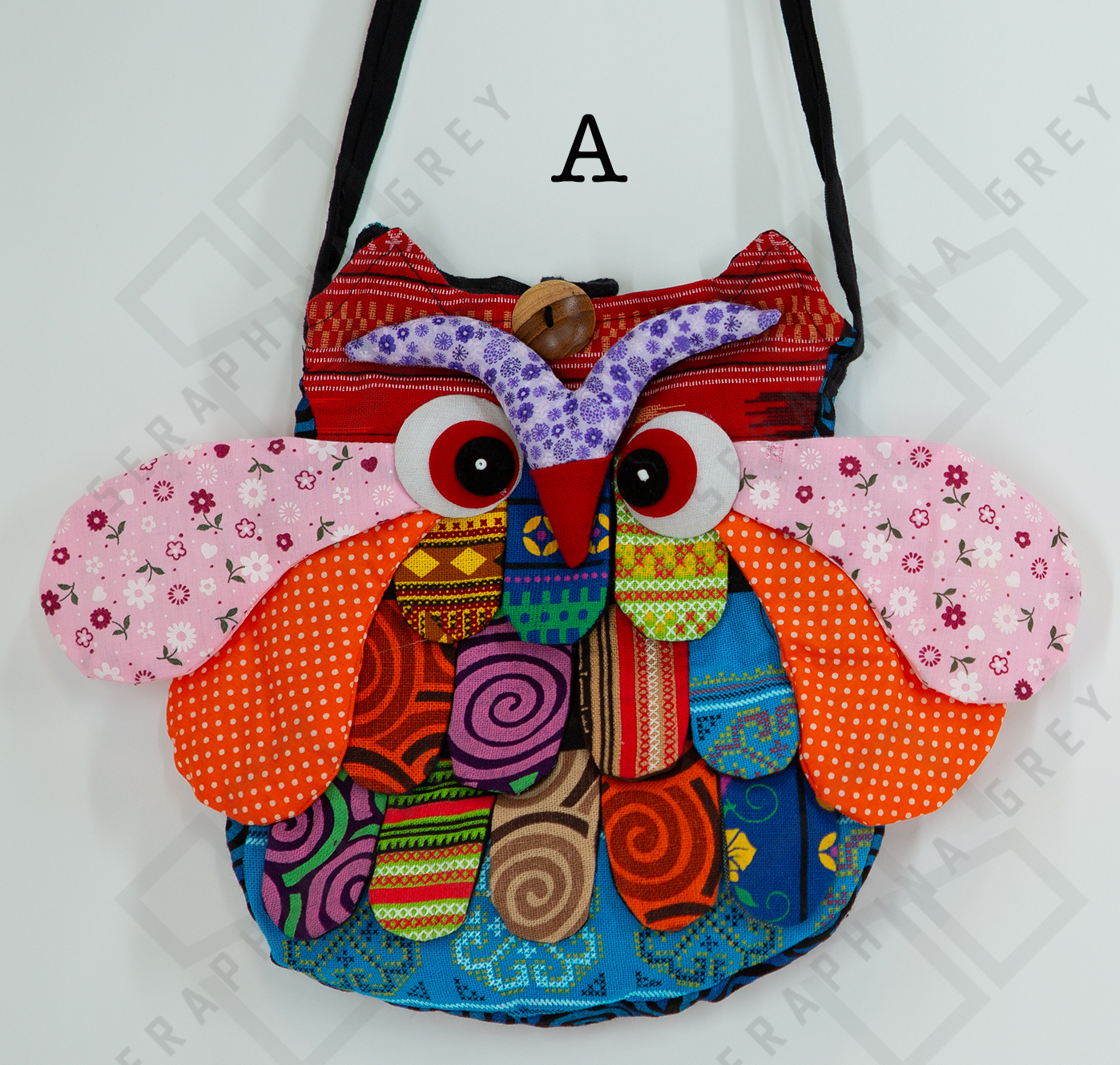 The image shows a close-up of a colorful handmade round owl handbag labeled “A.” The bag features a vibrant patchwork design with various patterns, including floral, polka dots, and geometric shapes in shades of orange, pink, purple, blue, and green. The owl’s large, expressive eyes and beak are prominently displayed, along with detailed wings and feathers. The bag is hung by a black strap against a white background, highlighting its whimsical and playful appearance.