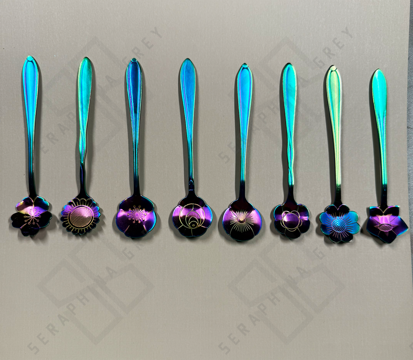 Set of rainbow colored decorative spoons with floral designs on a gray background