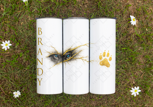 A personalized tumbler with a wolf's blue eyes design breaking through gold kintsugi cracks and a gold paw print. 