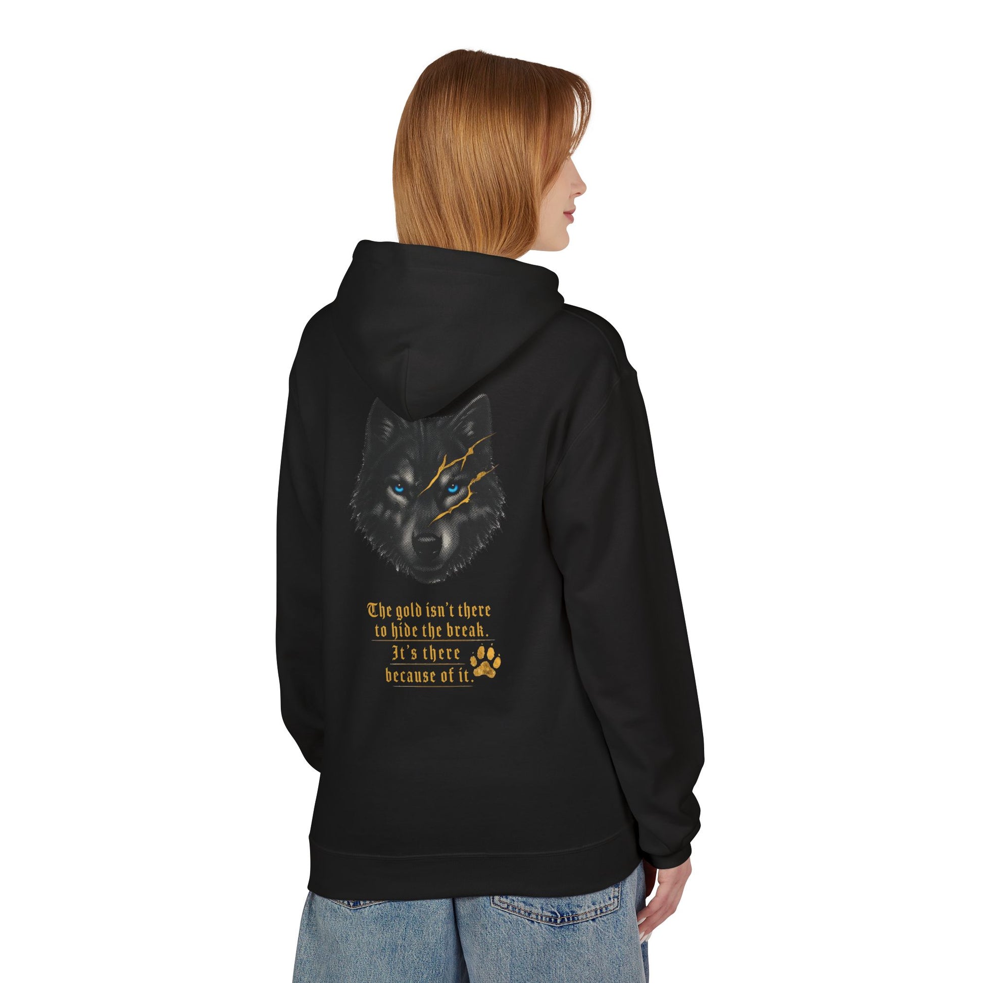 Black pullover hoodie worn by a model and shown from the back, featuring a wolf with bright blue eyes and gold kintsugi-style scars above the text, “The gold isn’t there to hide the break. It’s there because of it,” with a gold paw print below.