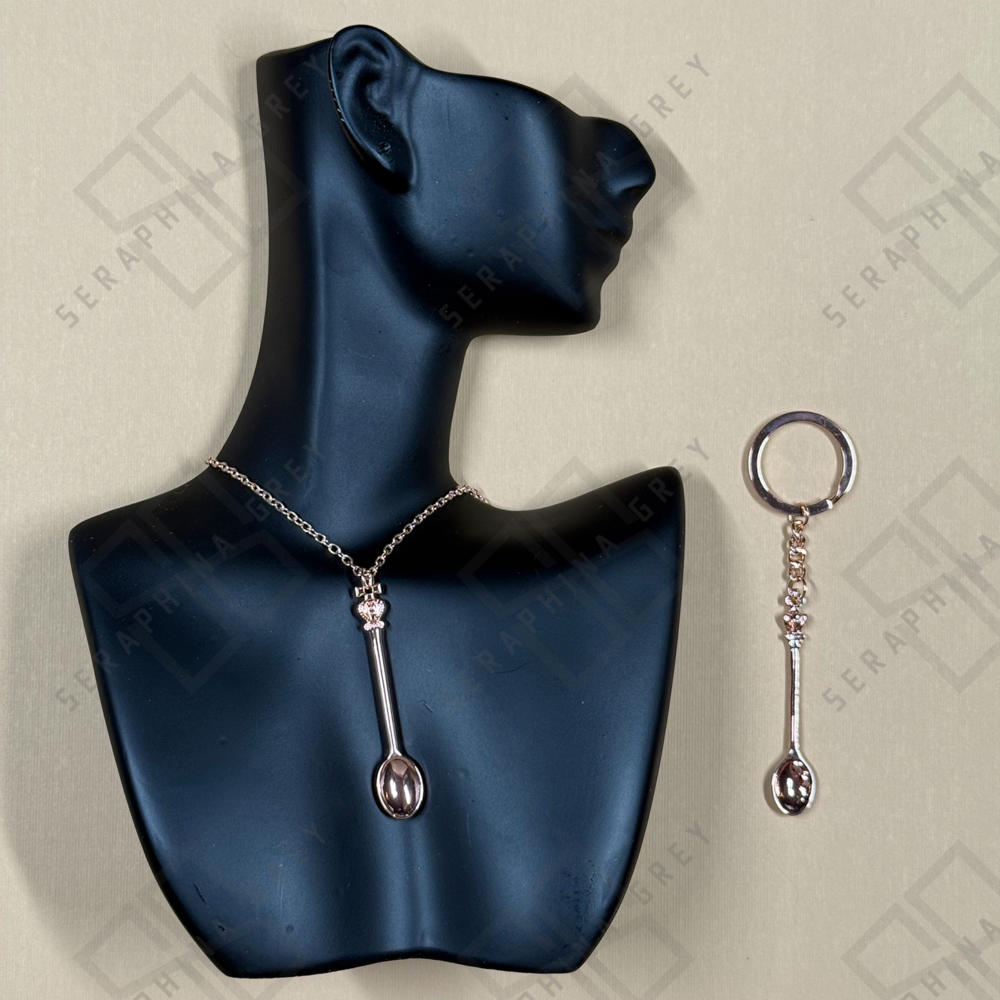 Rose Gold Spoon-shaped necklace and keychain on a black mannequin bust with a branded background.
