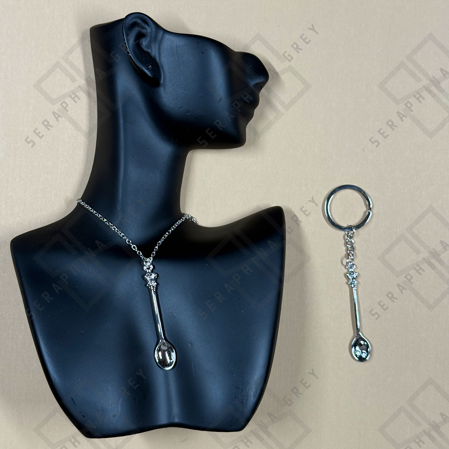 Silver Spoon-shaped necklace and keychain on a black mannequin bust with 'Seraphina' branding.