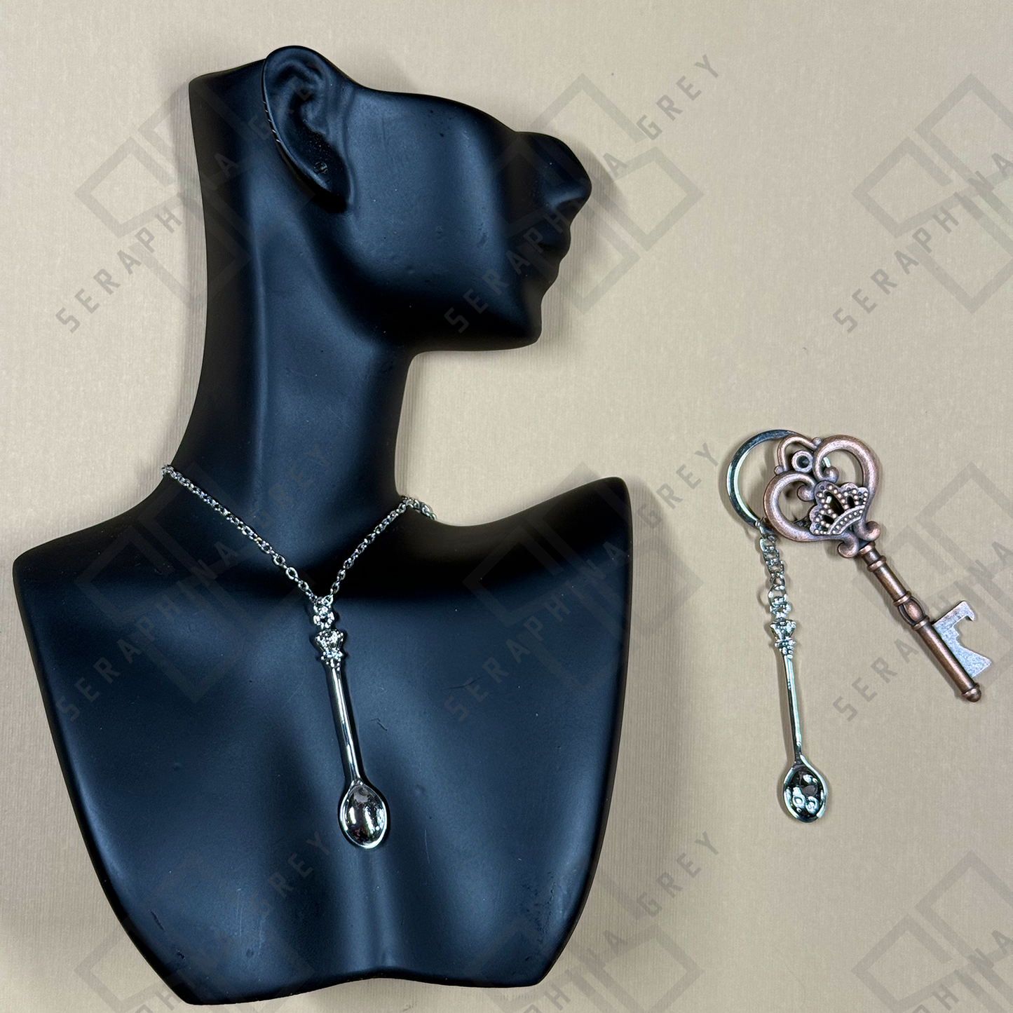 Silver Spoon-shaped necklace and keychain on a black mannequin bust with a branded background.