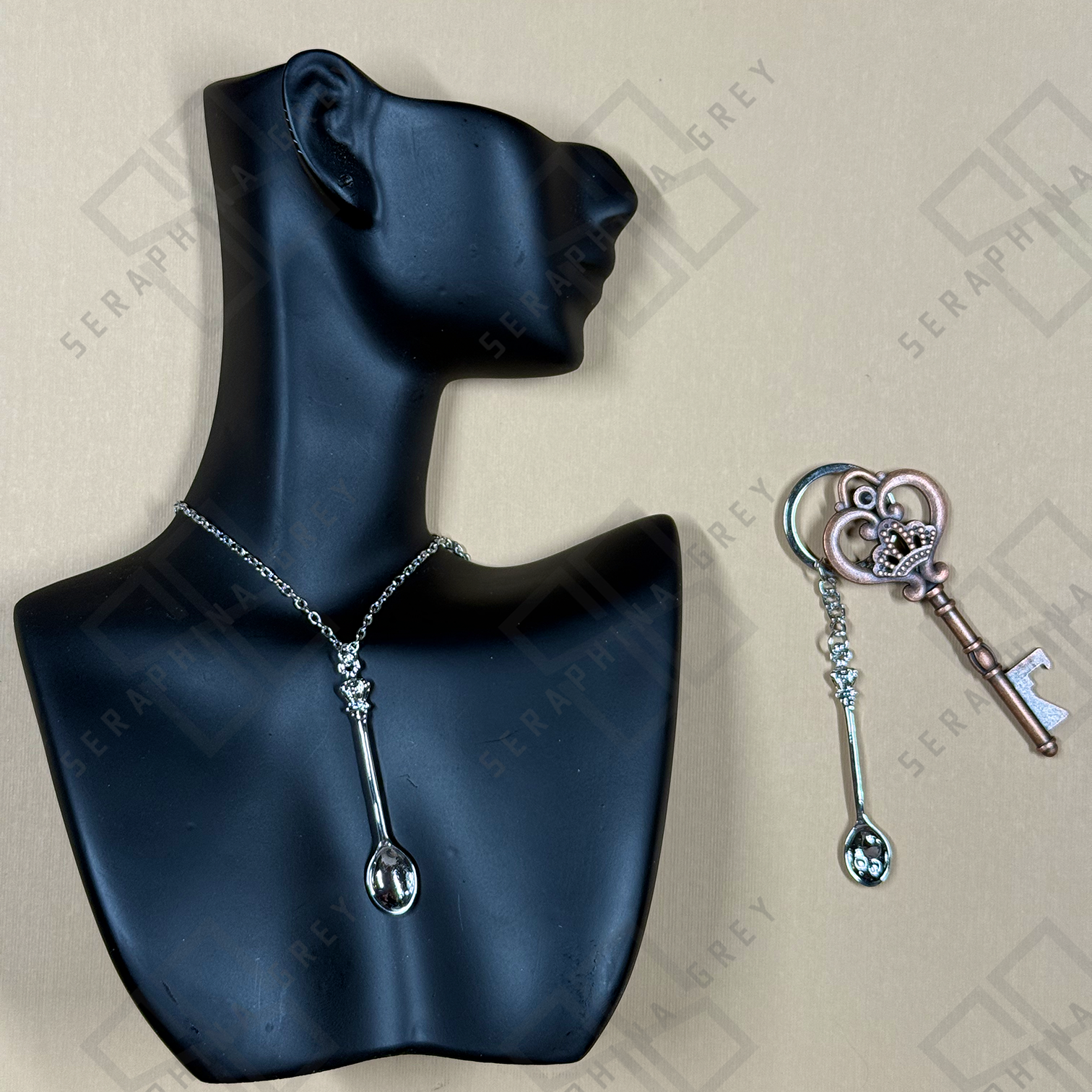 Silver Spoon-shaped necklace and keychain on a black mannequin bust with a branded background.