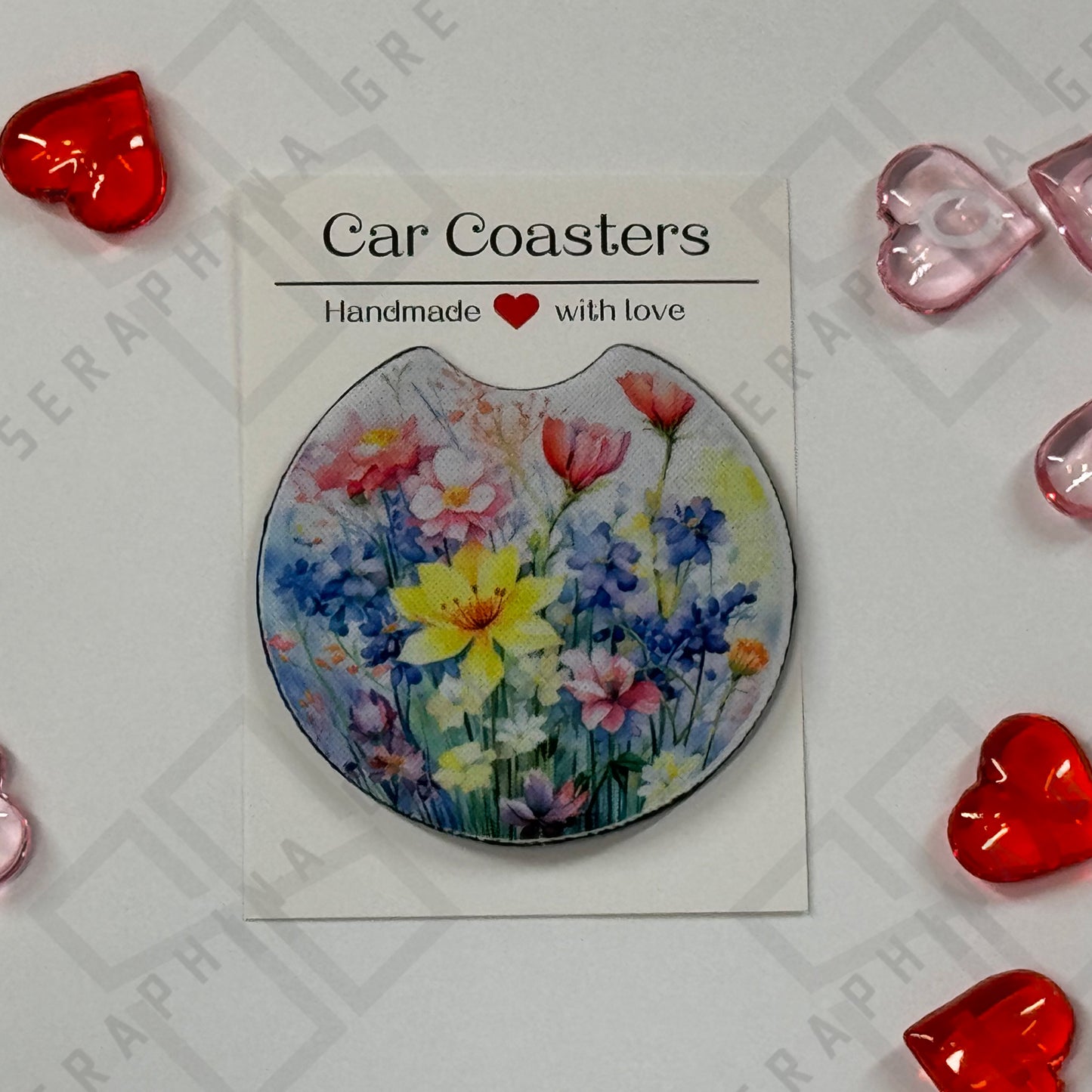 A single car coaster featuring a vibrant design of spring flowers, including yellow daffodils, pink tulips, and blue hyacinths, set against a soft pastel background. The coaster is accompanied by a label that reads ‘Car Coasters - Handmade with love.’ The display includes red and pink heart-shaped decorations around the edges