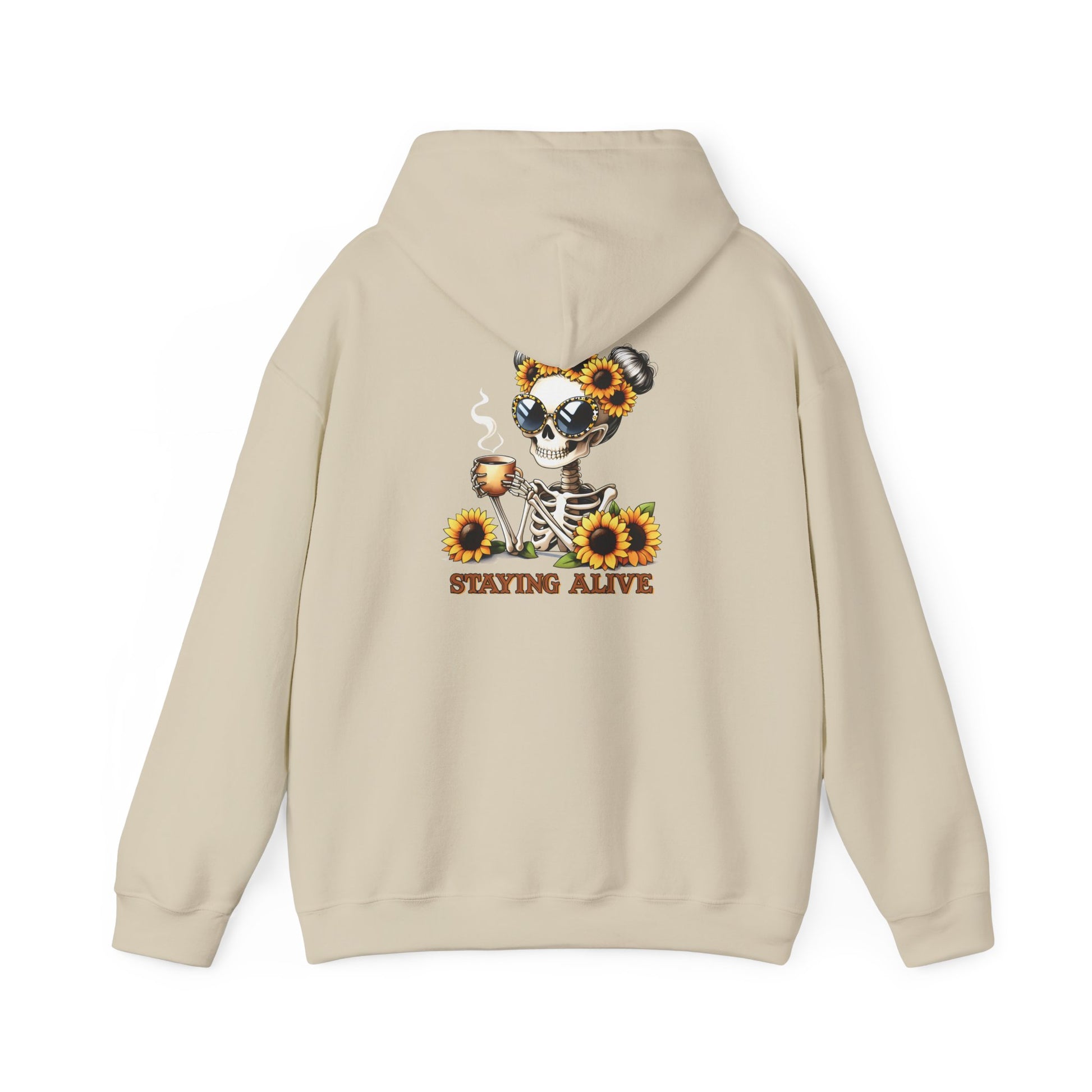 Sand-colored pullover hoodie shown from the back, featuring a skeleton wearing oversized sunglasses and sunflower space buns, holding a steaming mug, with “STAYING ALIVE” printed below.