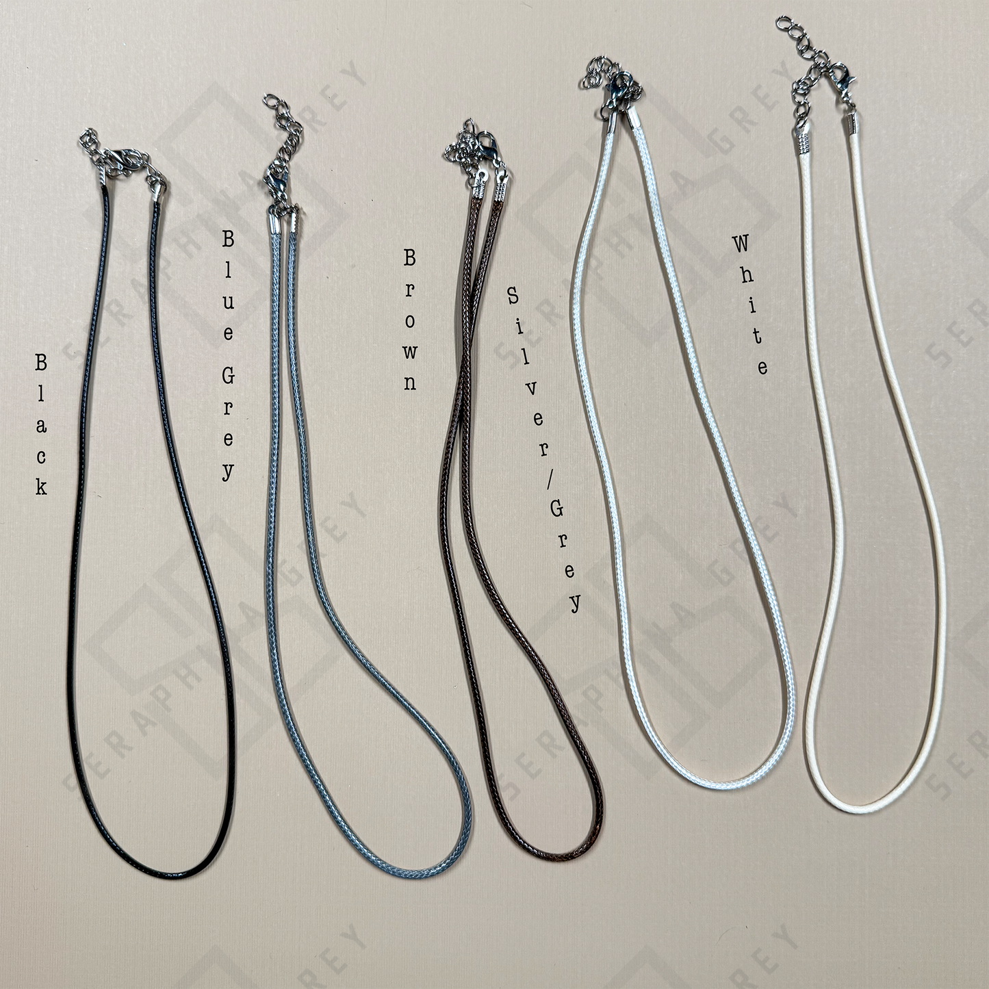 Five adjustable wax cord necklaces displayed side by side in black, blue-grey, brown, silver-grey, and white, each with silver-tone clasps and extender chains.