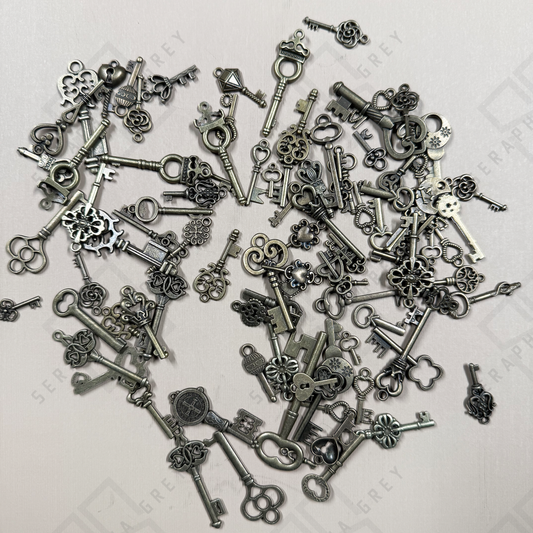 Assorted antique-style metal skeleton key charms in a variety of ornate shapes, sizes, and finishes, showing the range of key designs that may be selected for each handmade necklace.