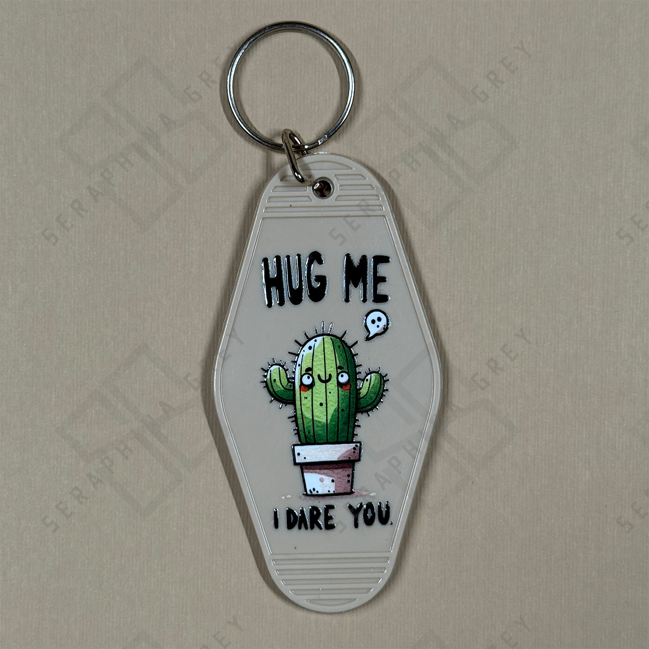 Keychain with a cactus design and text  hug me I dare you, on a beige background