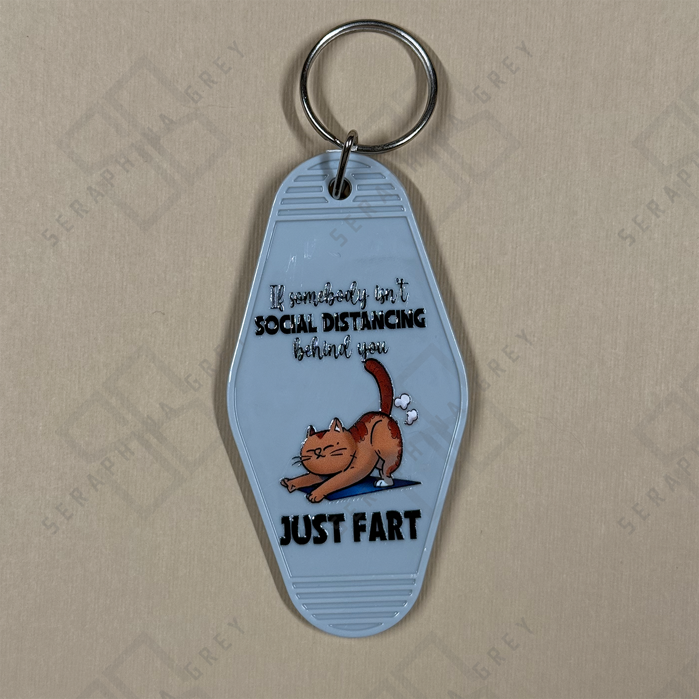 Keychain with a cat illustration and humorous text If someone cant sodical distance behind you just fart. on a beige background