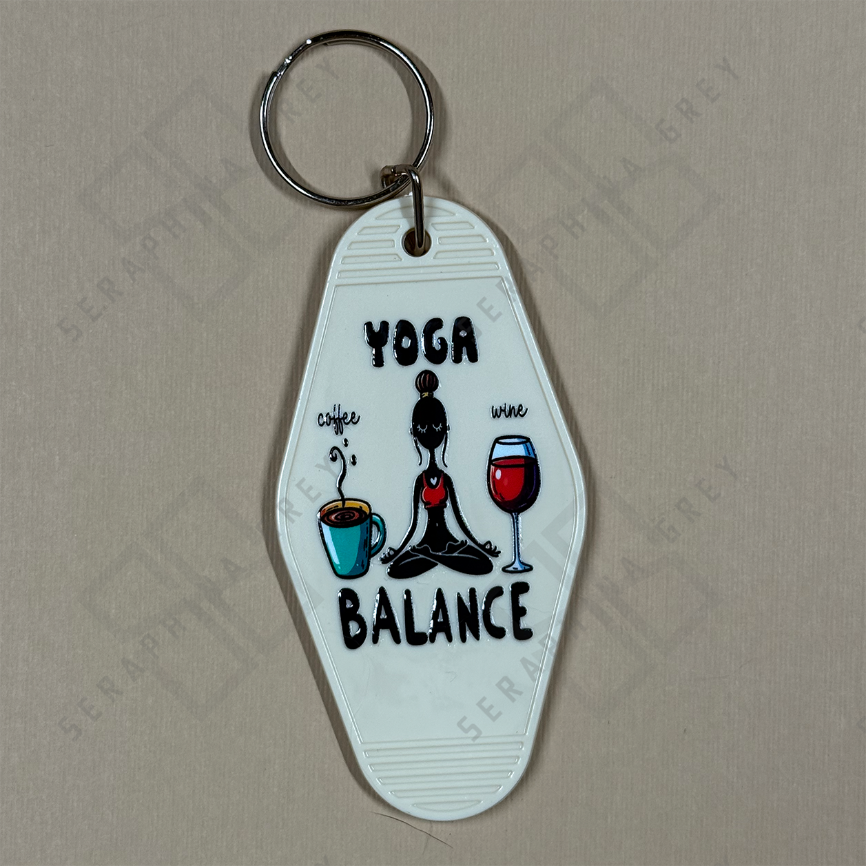 Keychain with yoga pose, coffee cup, and wine glass  and the text yoga balance on a beige background